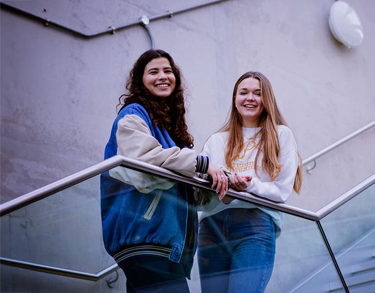 Two students stood on a stairwell smiling
