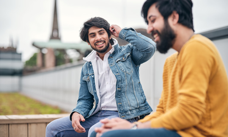 Two international students talking on The Hub rooftop garden witht he Coventry Cathedral ruins in the background.