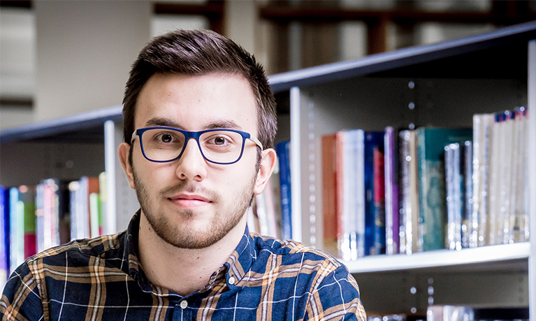 Male student sat in front of a bookshelf
