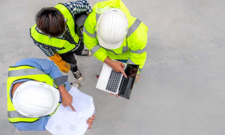 overhead image of men wearing hi vis vests looking at a laptop