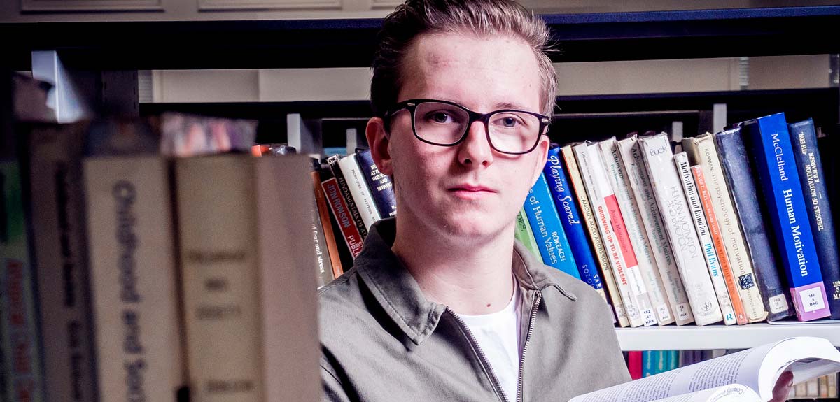 student stood in library, in front of books