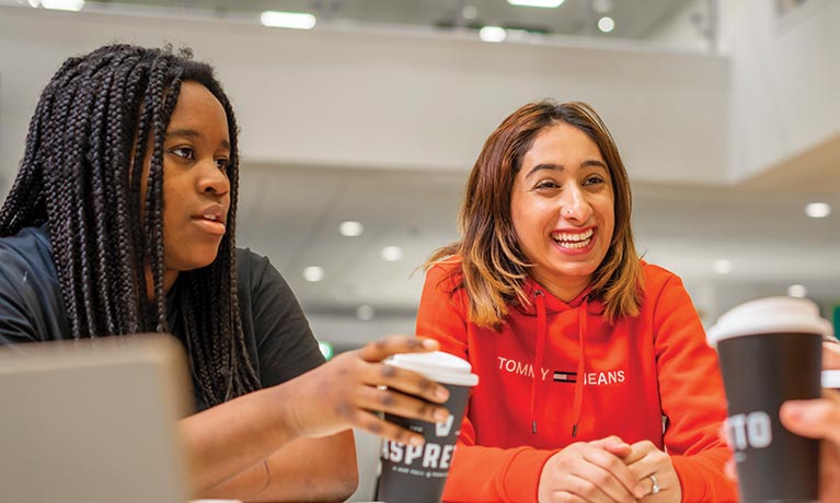 Two students talking whilst drinking a takeaway coffee