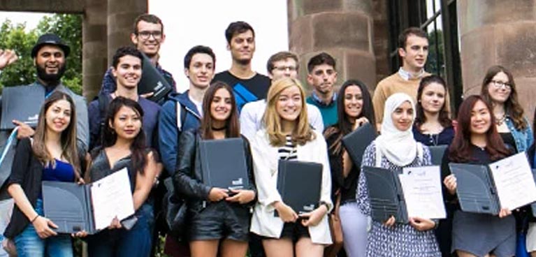 a group of students stood outside, smiling and holding folders