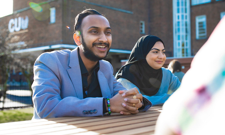Two students sat on a bench outside on a sunny day