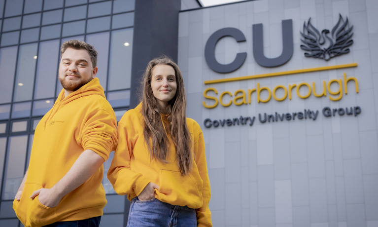 Two Scarborough students wearing bright yellow hoodies, stood outside the CUS building