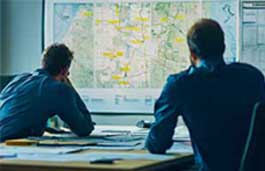 Two man looking at a large screen with a map 