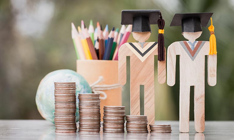 Wooden models on table with cap and gown, coins and pencils