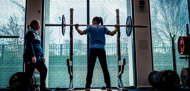 A woman lifting weights while another woman spots her.