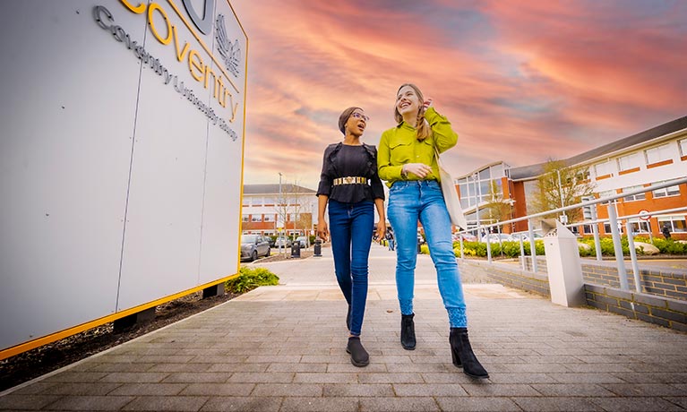 Two students walking next to Mile Lane with a colourful sunset 