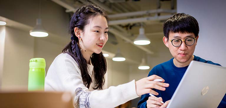 Two students chatting and looking at a laptop