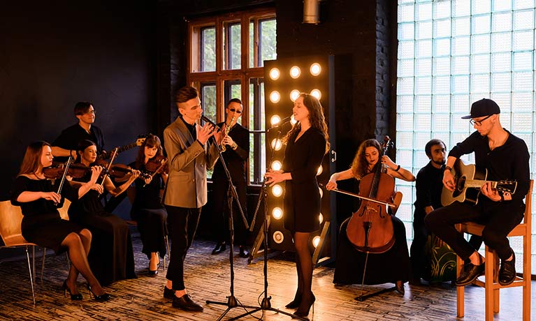 Group of musicians playing various instruments in the background behind with a male and female singers