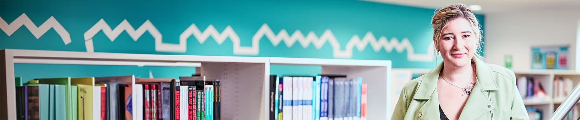 Female students leaning against a bannister standing in front of a shelf of books