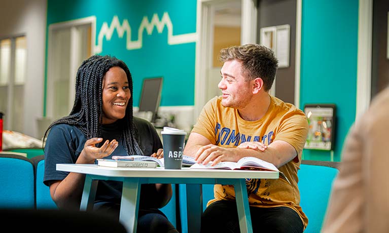 Two students sat at a table talking to each other