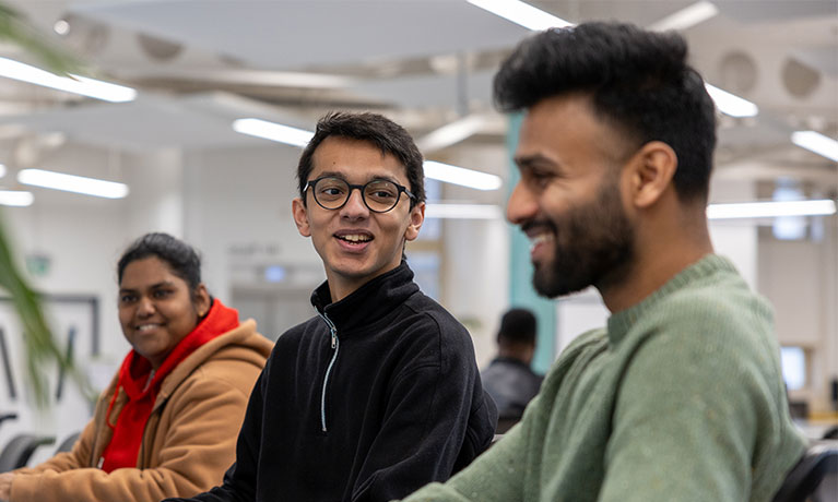 Three smiling students, two looking at the one nearest the screen