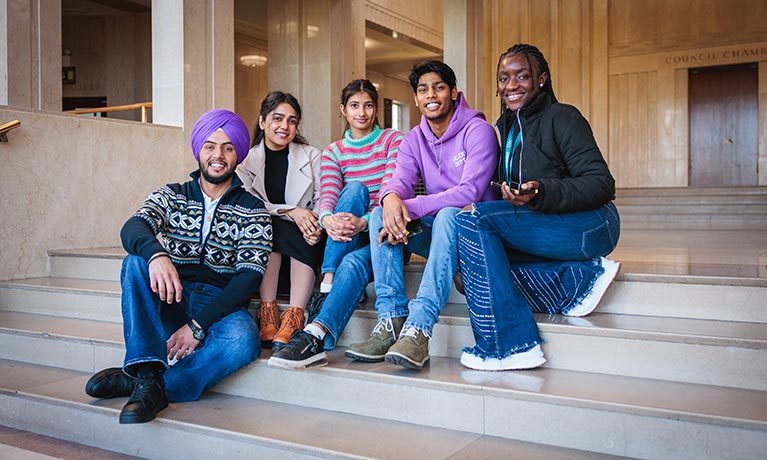 Group of students sat together on some steps smiling