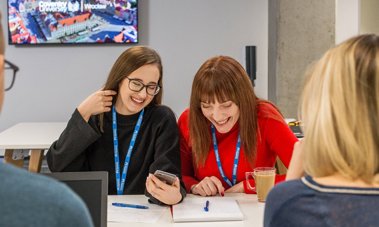 Students working in a group, smiling while looking at a smartphone
